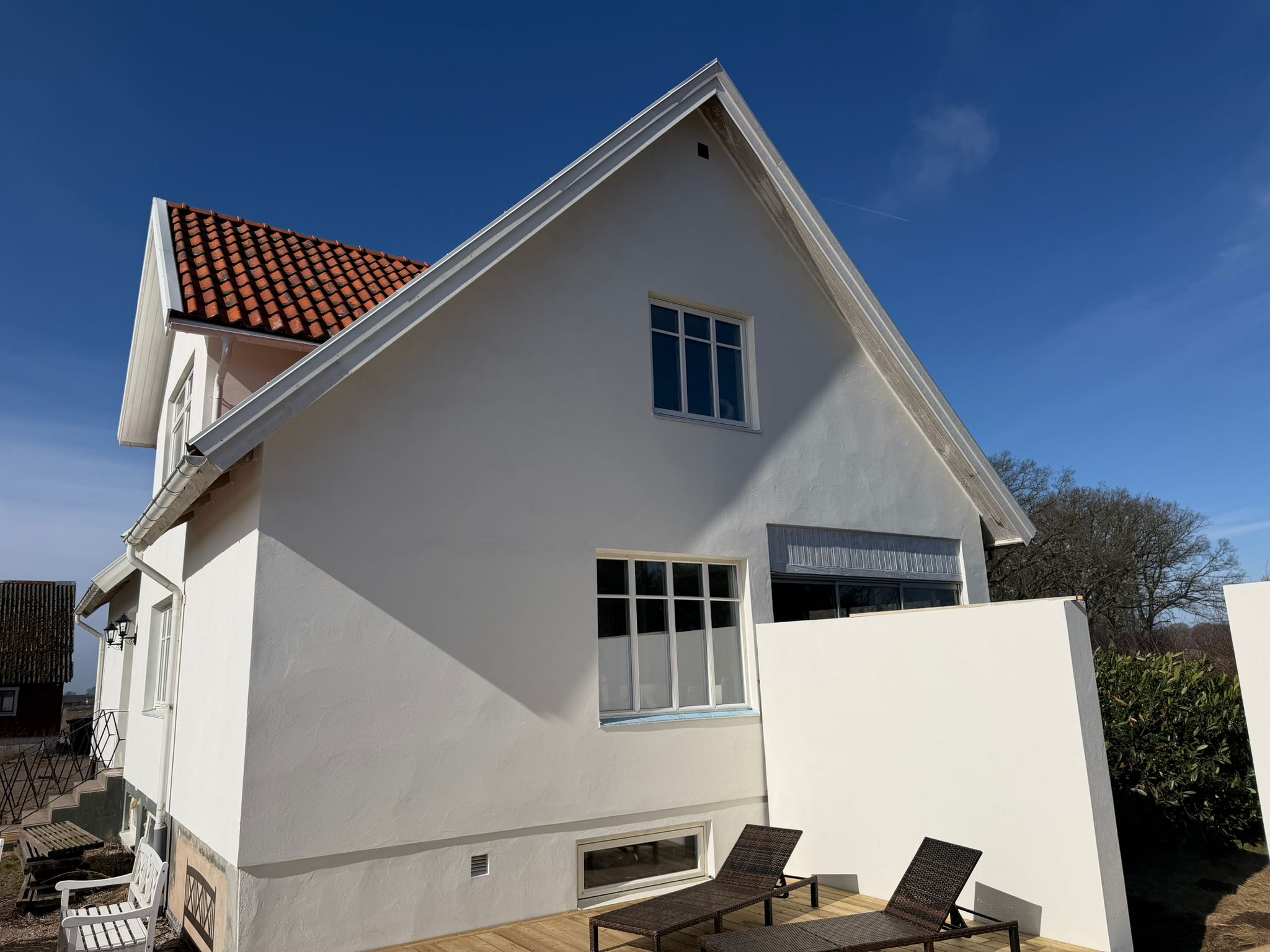 Vit putsad villa med blå himmel i Båstad efter komplett fasadrenovering
