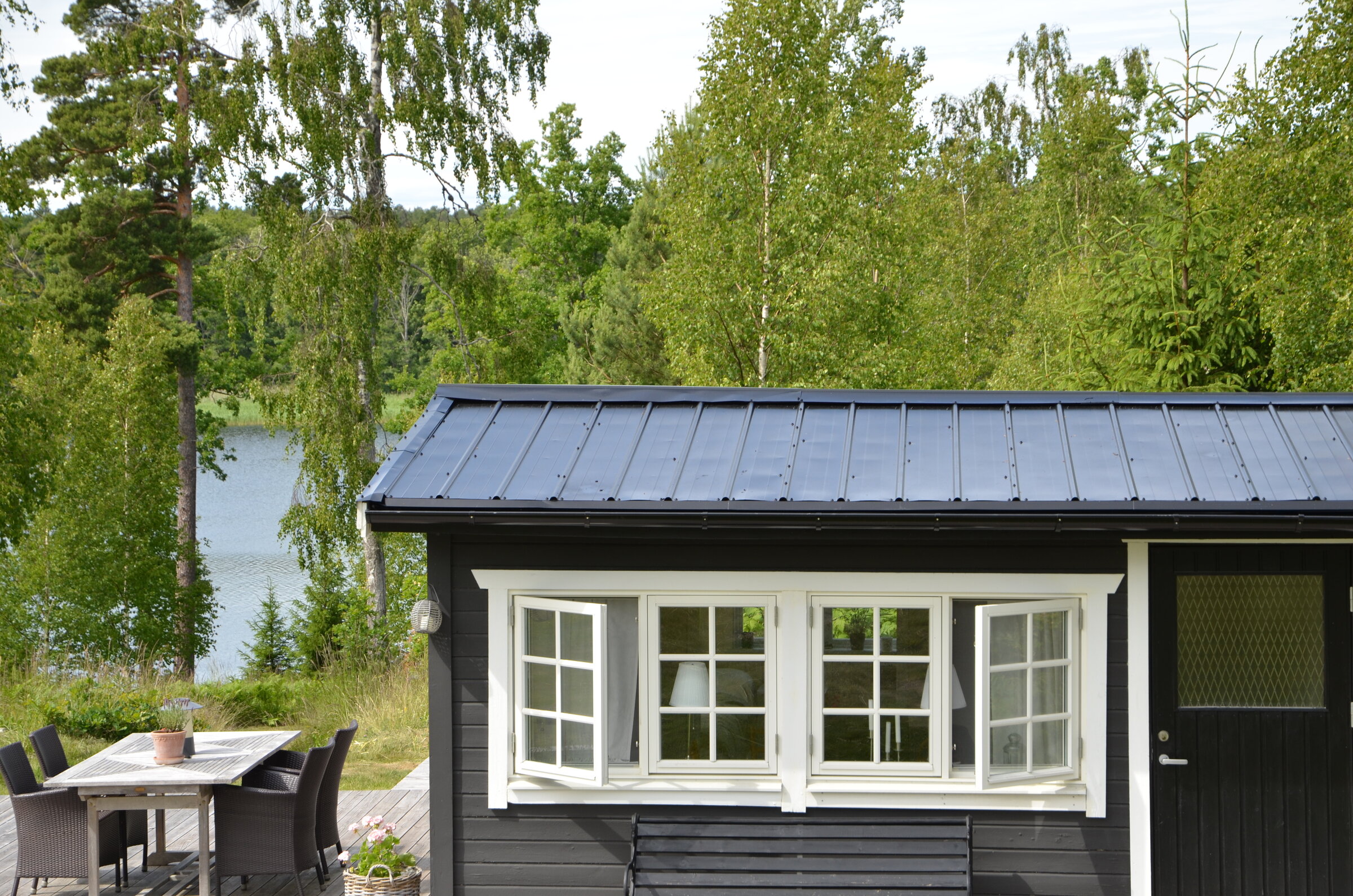 Svart stuga med mörkt pannplåtstak vid sjö, utförd av Arbetslag Bygg