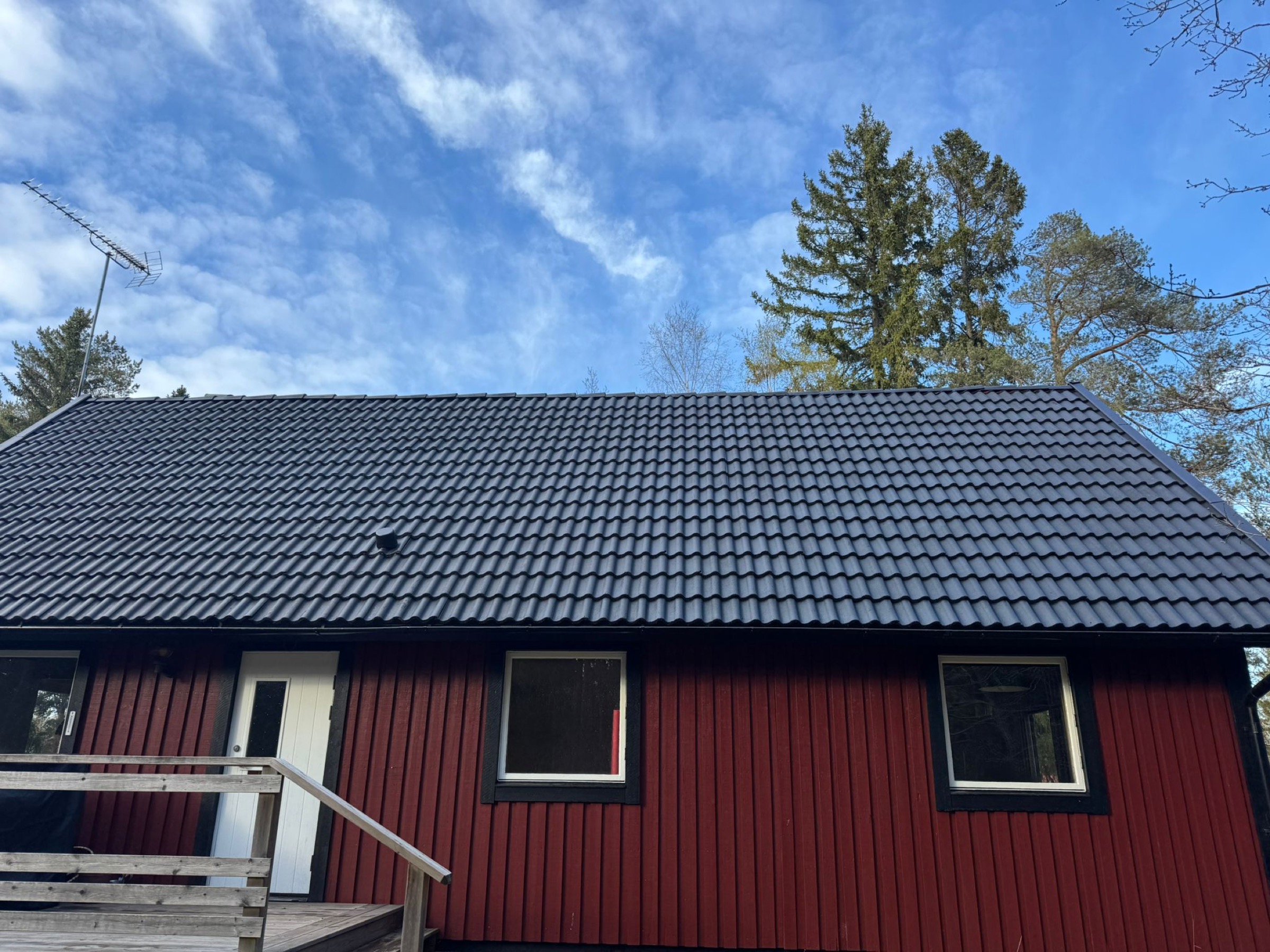 Mörkt, väl underhållet tegeltak på en röd villa, skött av Arbetslag Bygg
